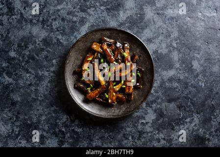 Rührbraten Bulgogi Aubergine auf Platte über dunklem Steinhintergrund mit freiem Textraum. Gebratene Aubergine im koreanischen Stil. Draufsicht, flaches Lay Stockfoto