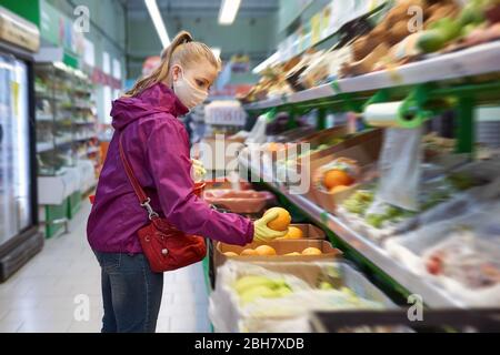 Frau in selbstgemachter Maske und Schutzhandschuhen kauft während eines Ausbruchs des Coronavirus COVID-19 in einem Supermarkt Obst Stockfoto