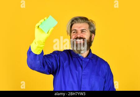 Frühjahrsputz-Service. Verwenden Schwamm für die Reinigung. Ehemann sauberes Haus. Hygiene und Reinheit. Bärtiger Mann tragen Gummihandschuhe. Reife Hausmeister in uniform gelbem Hintergrund. Stockfoto