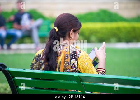 Ein indisches Mädchen, das in einem Park auf einer Bank sitzt und Mobile in indien verwendet Stockfoto