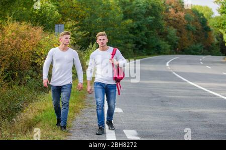 Wählen Sie Ort, wo Auto leicht zur Seite ziehen kann. Männer Rucksack zu Fuß Straße. Zwillinge gehen die Straße entlang. Adventure Concept. Jungs, die auf der Straße unterwegs sind. Automatischer Stopp für Reisende. Probleme werden transportiert. Stockfoto