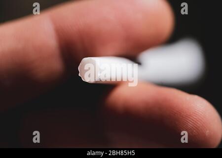 Geringe Schärfentiefe (selektiver Fokus) und Makrobild mit den Fingern eines Mannes, der eine gerollte Tabakzigarette hält. Stockfoto