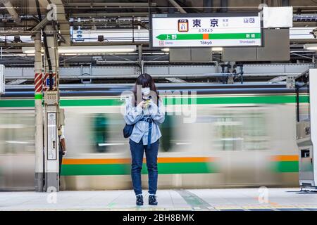 Japan, Honshu, Tokio, Tokyo Station, Yamanote Line Platform, Junge Frau mit Maske, die auf den Zug wartet Stockfoto