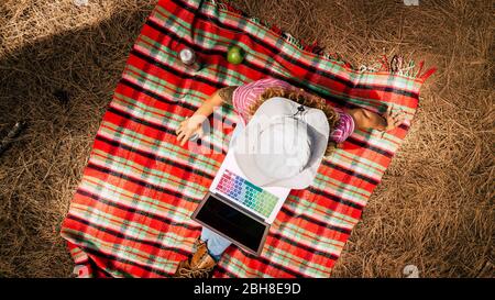 Draufsicht auf die Frau, die auf einem Laptop im Wald während der Reise oder im Urlaub arbeitet - alternative Büro und freie Freiheit Arbeit für moderne digitale Nomaden - rote Farben und Muster Hintergrund Stockfoto