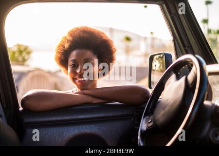 Junge schöne schwarze weibliche Reisende mit dem Auto off Road mit Sonnenlicht des Sonnenuntergangs hinter ihnen wie ein backgroiund. Sie lächeln Sie an. Schönheit und Rennen afro amerikanischen Konzept Stockfoto