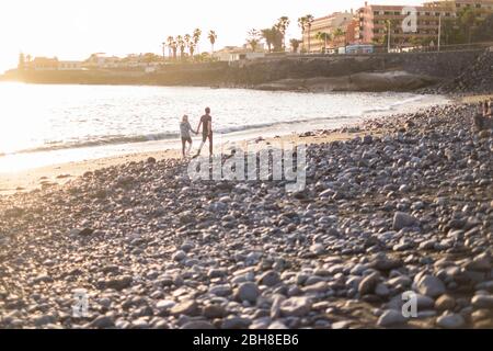 Romantisches Paar zu Fuß am Strand in der Nähe von Wellen und Flut. Felsen Strand für Familie und Menschen in der Liebe mit goldenen Sonnenuntergang im Hintergrund Stockfoto