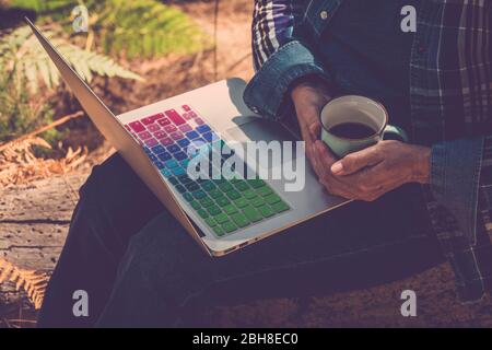 Nahaufnahme Frau im Freien mit Kaffeetasse und Notebook auf den Beinen bereit zu arbeiten und Internet-Verbindung - arbeiten überall ohne Altersbegrenzung für moderne freie Menschen mit Computer und WiFi-Signal Stockfoto