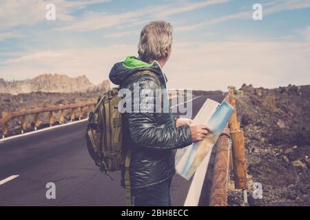 Portrait des Abenteuers Senior mit Karte und extreme Explorer Ausrüstung auf Berg mit langen geraden Straße vor ihm für einen langen Spaziergang. Fernweh und Reisekonzept Bild. Felsen und blauen Himmel landschaftlich Ort Stockfoto