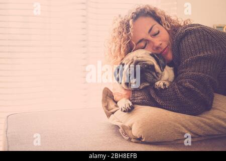 Romantische Dame umarmen seine beste Freundin alten Mops auf dem Sofa, die beide schlafen zusammen in Liebe und Freundschaft. Fensterlicht zu Hause - Lifestyle und Haustiertherapie Konzept - warme Brauntöne Herbst-Stil Stockfoto