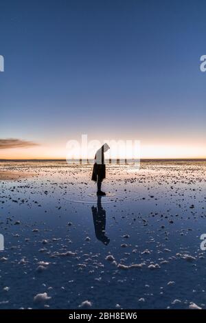 Mann steht auf seiner eigenen Reflexion auf Wasser in Salzebenen Stockfoto