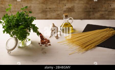 Niedrige Winkelansicht des typisch italienischen Rezept Spaghetti aglio olio e peperoncino (Knoblauch, Öl und Paprika) Zutaten mit einem Glas mit Sprigs Stockfoto