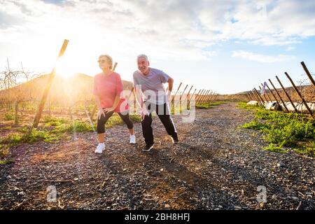 Zwei Erwachsene Männer und Frauen genießen Sport Fitness Aktivität im Freien in der Natur bei Sonnenuntergang tun Stretching und Balance Übung - Wellness und gesunde Lebensweise für ältere Paare Stockfoto