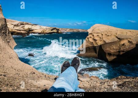 Reisen und entdecken Sie malerische Orte für Beine liegen und entspannen Sie sich auf einer Klippe mit blauen großen und gefährlichen Sturm Meer Wellen - Farben und Küste Aktivität im Urlaub Stockfoto