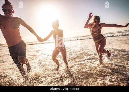 Freunde kaukasischen Gruppe von Menschen Mann und zwei Frauen genießen und Spaß zusammen in Freundschaft während Sommerferien aus dem Wasser laufen - Sonnenuntergang Sonne im Hintergrund mit klarem Himmel Stockfoto