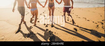 Rückansicht Menschen im Sommerurlaub laufen auf dem Sand am Strand zum Wasser Meer alle zusammen in Freundschaft Hand halten - Bikini-Gruppe Männer und Frauen haben Spaß in den Sonnenuntergang mit Schatten Stockfoto