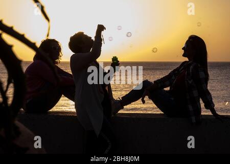 Freundschaft für Frauen während des Sonnenuntergangs - Emotion und Gefühl mit goldenen Farben und drei Damen in Silhouette mit Blasen Seife spielen - Urlaub und Outdoor-Freizeitkonzept Stockfoto