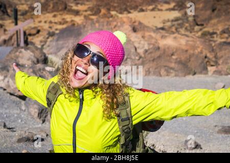 Junge schöne Frau lachen und lächeln mit freudigen und offenen Armen genießen Sie die alternative Wanderurlaub in Outdoor-Berge im Sommer - sonniger Tag und lustige rosa Hut für die kalte Temperatur Stockfoto