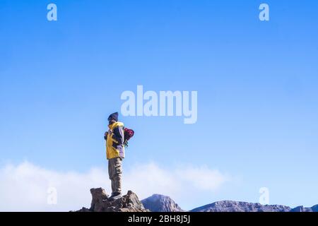 Wandermann stehend und auf der Bergspitze mit klarem blauen Himmel mit Wolken in Backgorund umblickend - Erfolg und Wanderkonzept Outdoor - Freizeitaktivitäten in der Natur Freiheit genießen Stockfoto