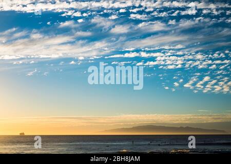 Sonnenuntergang am Meer mit einer Fährschifffahrt am Horizont und einigen Surfern auf dem Wasser warten auf einige Wellen, um zu trainieren und den aktiven Lebensstil mit Surf und Freiheit zu genießen Stockfoto