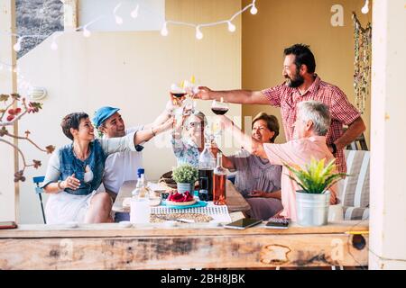 Gruppe von gemischten Alters und Generationen Freunde Familie haben Spaß zusammen klirren und Toasting während der Mittagszeit mit Essen und Getränken - fröhliche kaukasische Menschen lächeln und lachen zu Hause auf der Terrasse im Freien Stockfoto