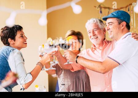 Glückliche Freunde, die Spaß im Freien haben - Junge und Alte genießen gemeinsam die Erntezeit - Freundschaftskonzept - Hände, die beim Abendessen zu Hause Rot- und Weißweinglas toasten - Glück und Feiern Stockfoto