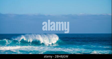 Big Wave Crash in der Mitte des Ozeans mit Klippen und Küste im Hintergrund - weißer Splash für große Schwellen und Gezeiten perfekt für Surfer - gefährliche blaue Ozean - Power Energy Stockfoto