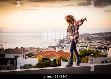 Lächelnde Frau Spaziergang in Balance über eine schöne Stadt Küste Meerblick bei Sonnenuntergang - Freiheit und Unabhängigkeit Glückskonzept für Menschen mittleren Alters genießen Outdoor-Freizeitaktivitäten über den Häusern Stockfoto