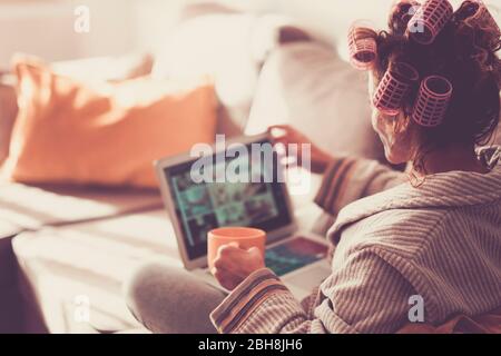 Lady von hinten mit einem modernen Technologie-Laptop zu Hause gesehen, während Lockenwickler auf seinem lockigen Haar - Farbtöne Vintage - Entspannung zu Hause trinken gesunden Tee - Frau mit Computer Stockfoto