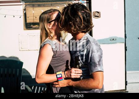 Junge schöne unkenntlich kaukasischen blonde Paar küssen und verlieben sich zusammen mit alten Vintage-Wohnwagen im Hintergrund- Urlaub und alternative Menschen Lifestyle-Konzept Stockfoto