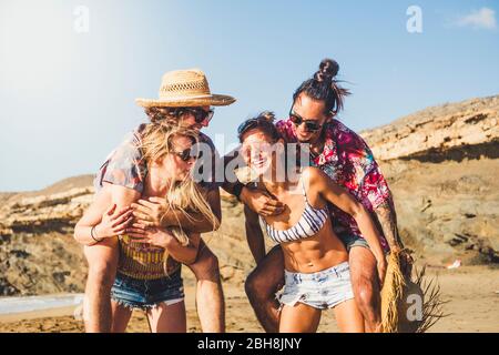 Fröhliche Menschen zwei Paare lachen und haben gemeinsam Spaß - Freunde genießen den Sommerurlaub im berach - Mädchen tragen Jungen - schöne junge Männer und Frauen spielen in glücklicher Freundschaft Stockfoto