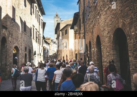 Menschenmenge von Touristen Menschen gehen zusammen gestreckt und mit der Straße voll in San Gimignano in der Nähe von Siena in der Toskana, Italien. Urlaub und Kultur in einer mittelalterlichen Stadt voller Geschichte Stockfoto