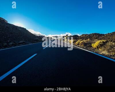 Lange Straße am Berg mit vulkan-Montierung vor und blauem, klarem Himmel - Bodensicht mit schwarzem Asphalt und weißen Linien - Fahr- und Reisekonzept Stockfoto