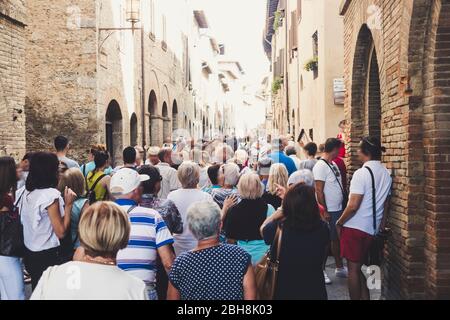 Menschenmenge von Touristen Menschen gehen zusammen gestreckt und mit der Straße voll in San Gimignano in der Nähe von Siena in der Toskana, Italien. Urlaub und Kultur in einer mittelalterlichen Stadt voller Geschichte Stockfoto