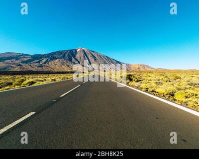 Lange Straße am Berg mit vulkan-Montierung vor und blauem, klarem Himmel - Bodensicht mit schwarzem Asphalt und weißen Linien - Fahr- und Reisekonzept Stockfoto