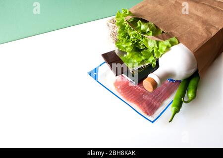 Lieferung von Lebensmitteln, kontaktlos, Einkaufen, Lebensmittelspende. Papiertüte Speck, Schokolade, grüne Chili, Salat, Olivenöl Botle. Stockfoto