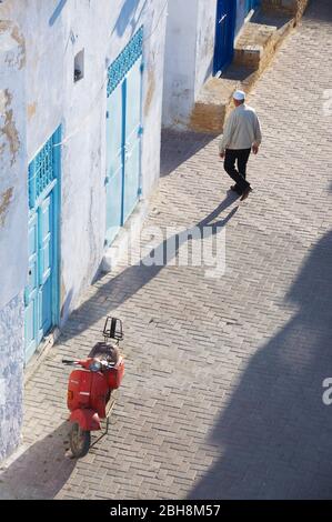 Ein alter roter Vespa Roller parkte auf einer Kopfsteinpflasterstraße in Kairouan, Tunesien vor einem alten traditionellen Gebäude mit einer hellblauen Holztür. Stockfoto