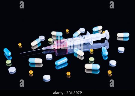 Medizinische Kunststoff 5 ml Spritze mit roter Flüssigkeit (Blut) und verschiedenen bunten Pillen, Tabletten und Kapseln auf schwarzem Hintergrund mit Reflexion gefüllt Stockfoto