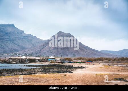 Geheimnisvolle Landschaft mit sandigen Küste mit Fischerdorf und schwarzen vulkanischen Bergen im Hintergrund. Baia Das Gatas. Nördlich von Calhau, Sao Vicente Island Kap Verde. Stockfoto