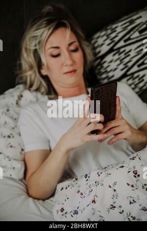 Frau liegt mit Smartphone im Bett Stockfoto