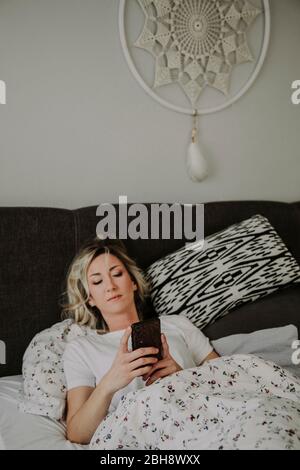Frau liegt mit Smartphone im Bett Stockfoto