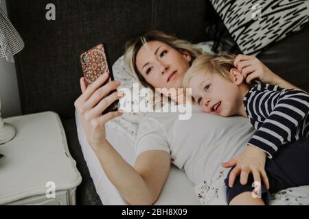 Mutter und Sohn mit Smartphone im Bett Stockfoto