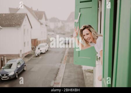 Frau blckt fröhlich aus dem Fenster, winkt Stockfoto