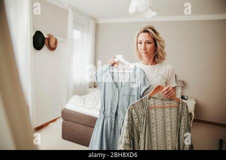 Frau steht vor dem Spiegel, kleidet sich unentschlossen Stockfoto