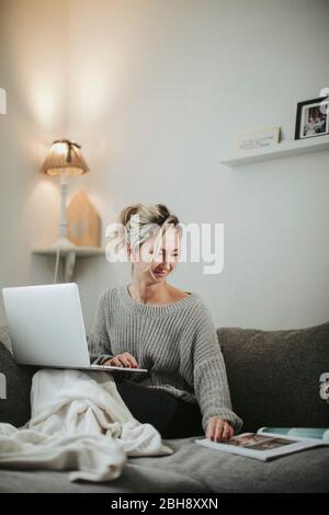 Frau sitzt spannend mit Laptop und Zeitschrift auf der Couch Stockfoto