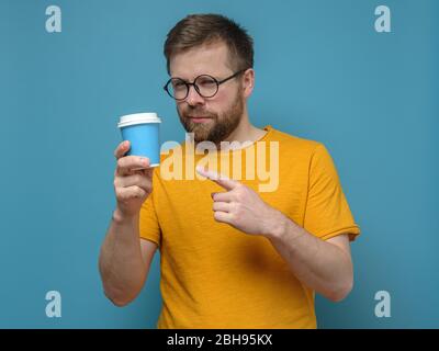 Der Mann zeigt mit Zeigefinger auf eine Papiertasse, die er in der Hand hält. Konzept der Pflege der Umwelt. Stockfoto