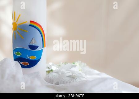 Taufkerze mit Fisch-, Schiff- und Regenbogenmotiv, Taufkleid und weißen Babyschuhen Stockfoto