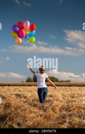 Junge Frau mit bunten Luftballons im Maisfeld gemähen Stockfoto