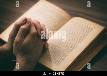 Gebet, Mann überreicht ein offenes Buch Heilige Bibel, hölzerner Schreibtisch Hintergrund. Konzept von Glaube, Religion und Spiritualität Stockfoto