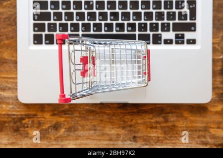 Online-Shopping im Internet, E-Commerce-Konzept. Warenkorb auf einem Computer Laptop, Holz Schreibtisch Hintergrund, Draufsicht. Stockfoto