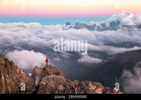Einsamer Mann steht auf einem Bergrücken, im Hintergrund ein Wolkenmeer rund um die Agner Bergkette, Pale di San Martino Gruppe, Blick vom Costabella-Grat, Dolomiten, Italien Stockfoto